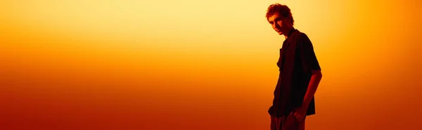 A young man poses confidently against a stunning orange sunset in stylish attire. — стокове фото