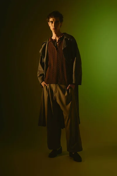 Handsome young man stands confidently in stylish attire against a vibrant green background. - foto de stock