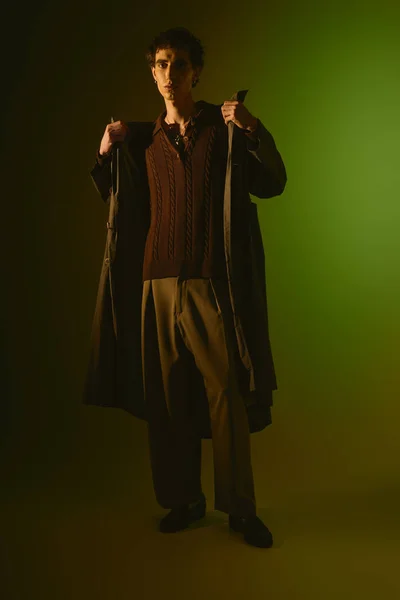 A stylish young man stands confidently, bathed in striking green light. - foto de stock