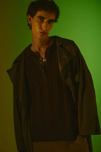 A young man dressed in trendy attire poses confidently against a striking green backdrop. — стоковое фото