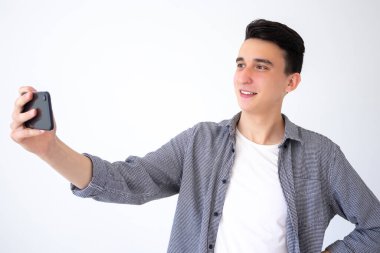 Olumlu, mutlu bir adam telefonuyla fotoğraf çeker ya da video bağlantısı ile iletişim kurar. Gri arka plandaki adam