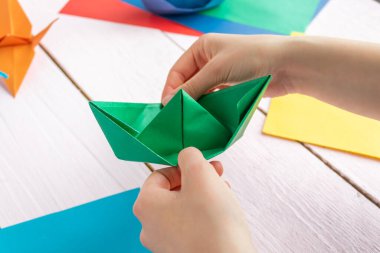 Bir kız origami vinci ve renkli kağıttan yapılmış bir tekne yapıyor. Ahşap bir arka planda