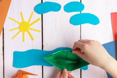 Bir kız kendi yaptığı origami oyuncağıyla oynuyor. Origami teknesi renkli kağıttan yapılmıştır.