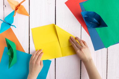 Bir kız origami yapmak için renkli kağıt katlar. Bir kız tahtadan bir masada origami yapıyor.