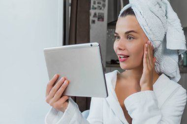 Beyaz havlu ve bornozlu güzel bir kadın elinde bir tablet tutuyor. Bir kadının sabah konsepti..