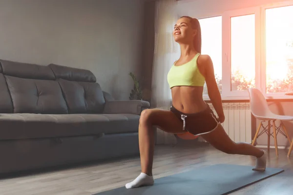 Genç beyaz kadın evde yoga minderinin üzerinde geriniyor. Ev konseptinde egzersiz.