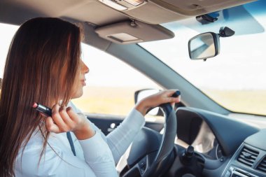 Güzel bir iş kadını araba sürüyor ve dudaklarını boyuyor.. 