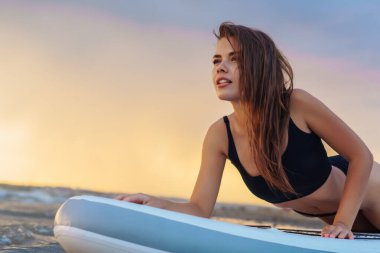 Sörf tahtasında uzanmış gün batımını seyreden genç seksi kadın sörfçü. Doğa kavramında dinlenme