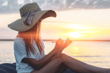 Hasır şapkalı genç kadın sahilde şiir yazıyor. İlham konsepti 