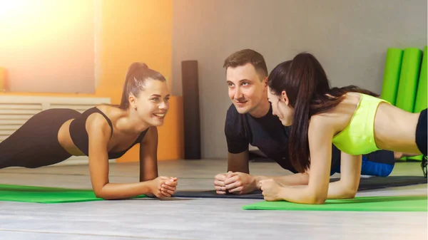 İki beyaz kadın ve erkek fitness stüdyosunda kalas yapıyor. Sağlıklı yaşam tarzı kavramı. Grup eğitimi