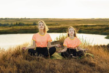 Genç anne ve kızı aynı kıyafetlerle dışarıda yoga yapıyor.. 