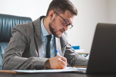 Gözlüklü genç işadamı ofisinde çalışıyor..