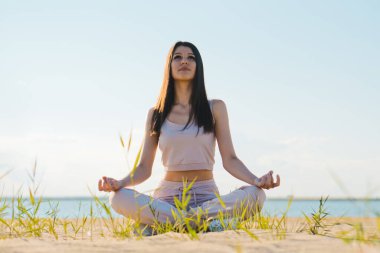 Gül eşofmanlı hoş bir kadın sahilde yoga yapıyor..
