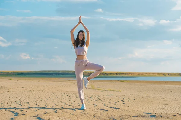 Gül eşofmanlı hoş bir kadın sahilde yoga yapıyor..