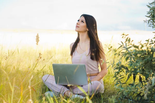 Young nice woman working on a laptop in yellow field. Working in nature concept.