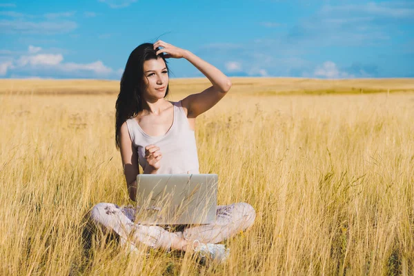 Young nice woman working on a laptop in yellow field. Working in nature concept.