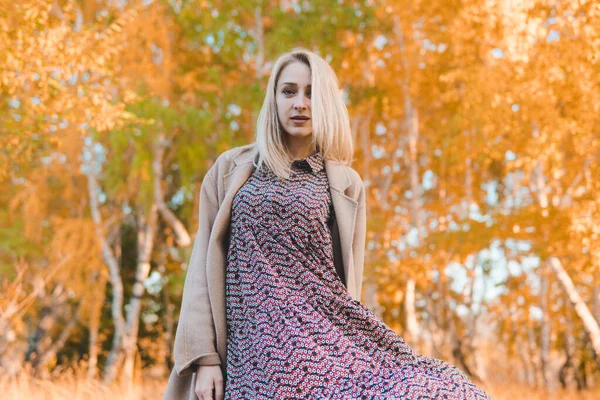 Young beautiful woman in long coat whirling in autumn forest. Autumn concept.