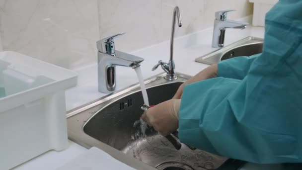 O tiro médio do doutor lava a ferramenta médica com uma escova abaixo de uma água corrente — Vídeo de Stock