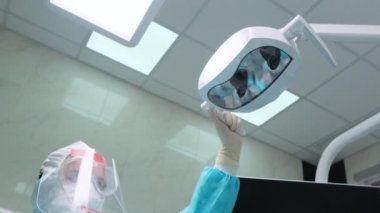 Kadın asistan, müşterinin dişlerini kontrol etmeden önce ışıklandırmayı ayarlar