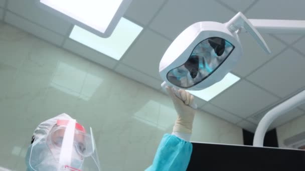 Assistente mulher ajusta a iluminação antes de verificar os dentes do cliente — Vídeo de Stock