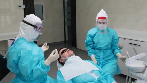 O paciente em óculos pretos sobe em uma cadeira dentária após procedimentos médicos — Vídeo de Stock