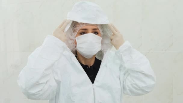 De arts in een wit beschermend masker trekt aan de capuchon en ritst de jurk dicht — Stockvideo