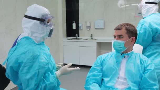 Hasta dişçiyi dinliyor. Yardımcı arka plandaki eldivenleri çıkarır — Stok video