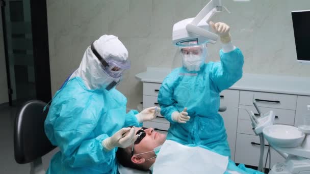 Mulher dentista com a ajuda de assistente trabalha com um paciente em consultório odontológico — Vídeo de Stock