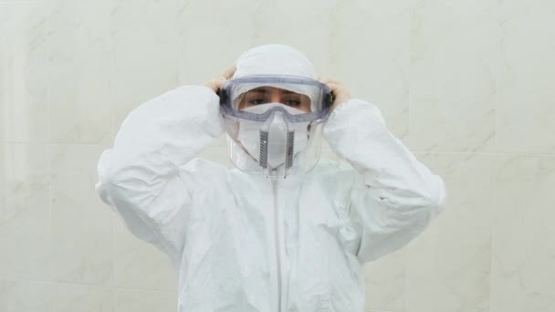 De arts in een wit beschermend pak met capuchon zet een groot plastic masker op — Stockvideo