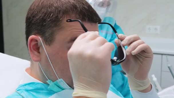 Close-up van de mannelijke cliënt draagt een zwarte bril en valt in een tandartsstoel — Stockvideo