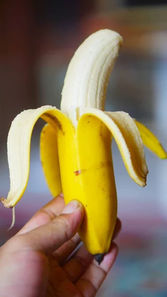 Kısmen soyulmuş sarı bir muzu tutan el.