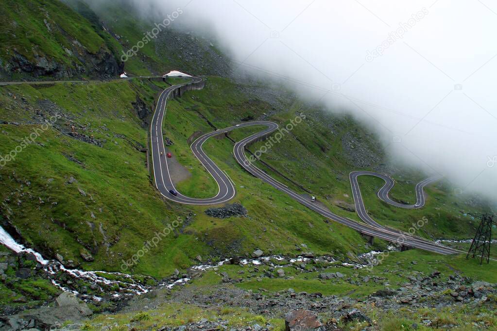 Transfagarasan road in the Balea river valley, Romania. Winding road that runs along the Balea river under a blanket of clouds on a rainy summer day.