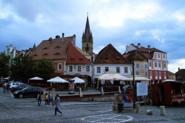 Sibiu / Romanya; 06 / 29 / 2018. Küçük Meydan 'daki restoranlar. Saint Mary 'nin Lüteryen Katedrali' nin çan kulesi arka plandaki çatıların üzerinden geçiyor..