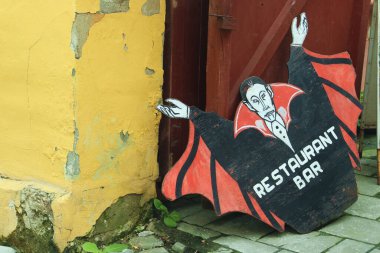 Sighisoara / Romanya; 06 / 30 / 2018. Sighisoara 'daki Tinsmiths Caddesi' ndeki restoran tabelası (Rumence: Strada Cositorarilor). Eski bir tahta Drakula tabelası eski bir restoranın yanında terk edilmiş..