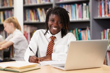 Portrait Of Female High School Student Wearing Uniform Working At Laptop In Library clipart