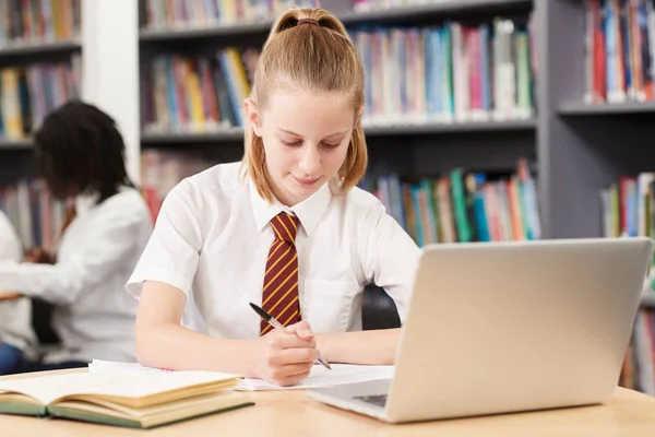 女中学生穿着校服在图书馆的笔记本电脑上工作 — 图库照片