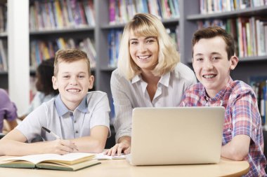Kütüphane içinde Laptop çalışan Bayan öğretmen yardımcı iki erkek lise öğrenci portresi