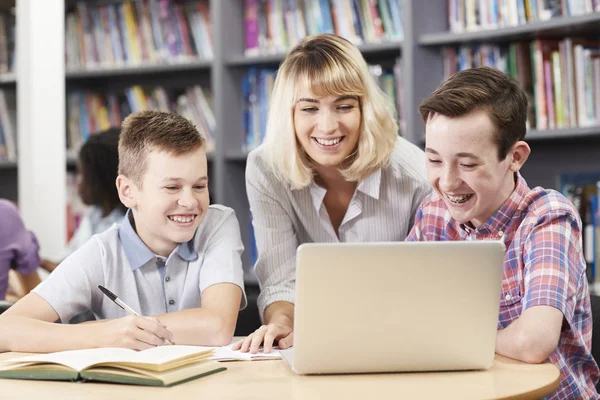 Kvinna Lärare Att Hjälpa Två Manliga Gymnasieelever Arbetar Laptop Biblioteket — Stockfoto