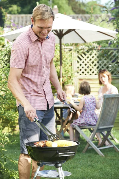 Father Cooking Barbeque For Family In Garden At Home