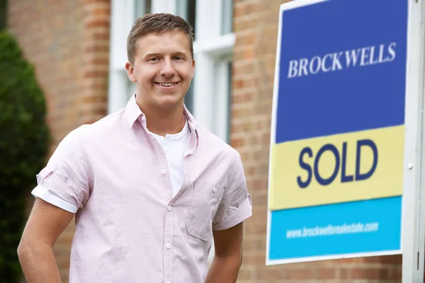 Lächelnder Mann steht vor neuem Haus mit verkauftem Schild — Stockfoto