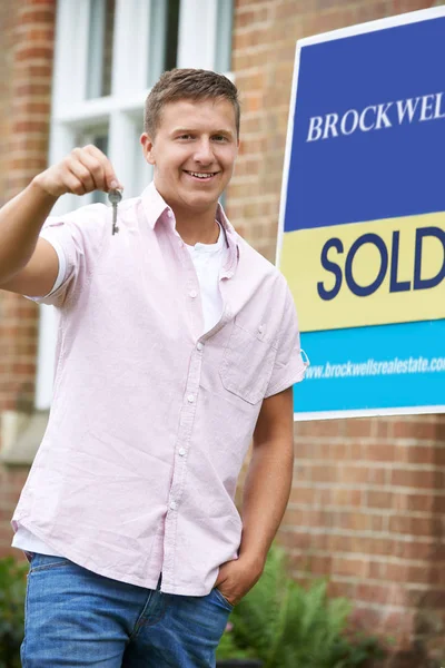 Porträt eines aufgeregten Mannes, der mit verkauftem Schild vor seinem neuen Zuhause steht — Stockfoto
