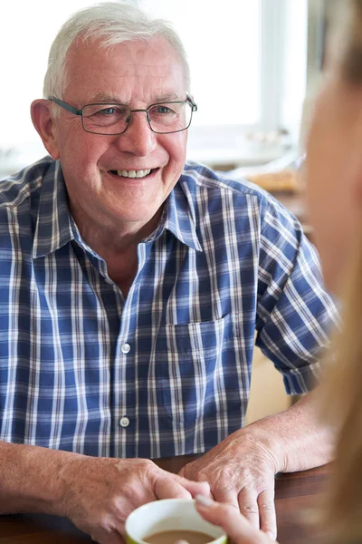 Homme âgé souriant assis dans la cuisine parlant avec une femme à la maison — Photo