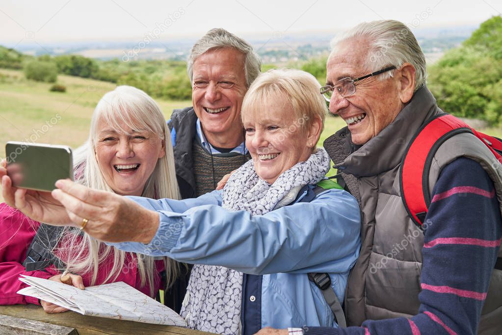 Group Of Senior Friends Hiking In Countryside Standing By Gate  