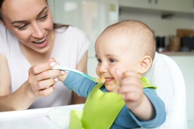 Gülümseyen 8 aylık erkek bebek evde mama sandalyede Besleniyor Sol