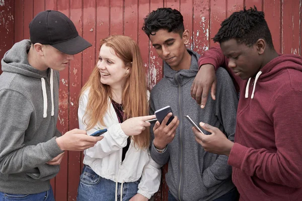 Grupa nastoletnich przyjaciół patrząc na telefony komórkowe w Urban setti — Zdjęcie stockowe