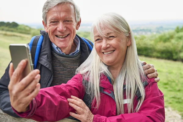 Usmívající se starší dvojice pěší turistika v krajině stojící u brány — Stock fotografie