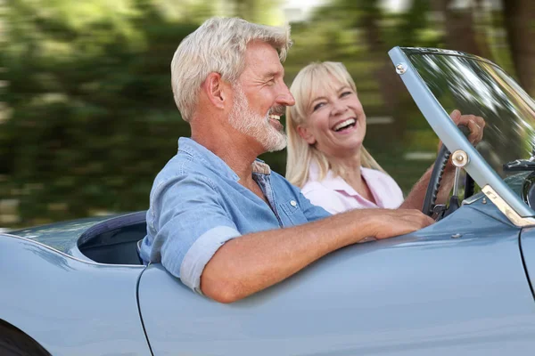 Pareja madura disfrutando de un viaje por carretera en un clásico coche deportivo abierto — Foto de Stock