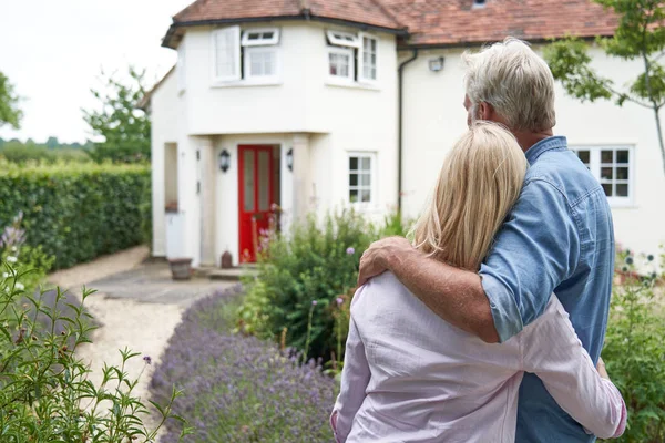 Rückansicht eines reifen Paares, das im Garten steht, Blick auf sein Traumhaus — Stockfoto