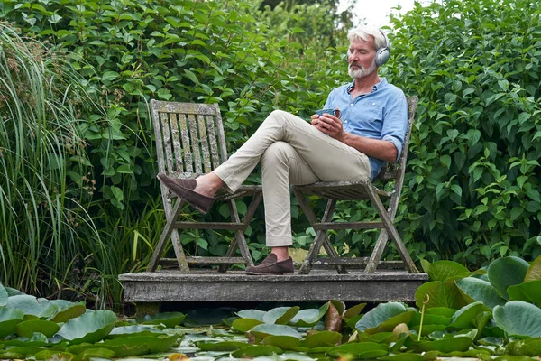 Зрелый человек расслабляется в саду, слушая музыку по беспроводной связи Hea — стоковое фото