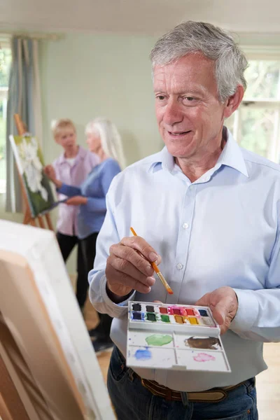 Старший чоловік відвідує клас живопису з вчителем на задньому плані — стокове фото